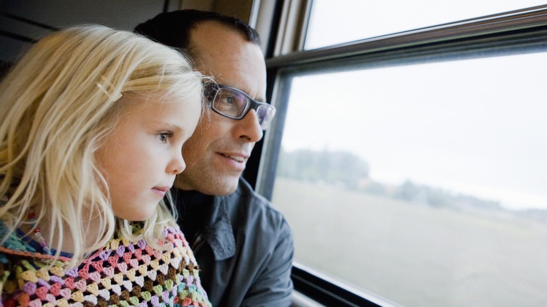 En flicka och hennes pappa tittar ut genom ett tågfönster.