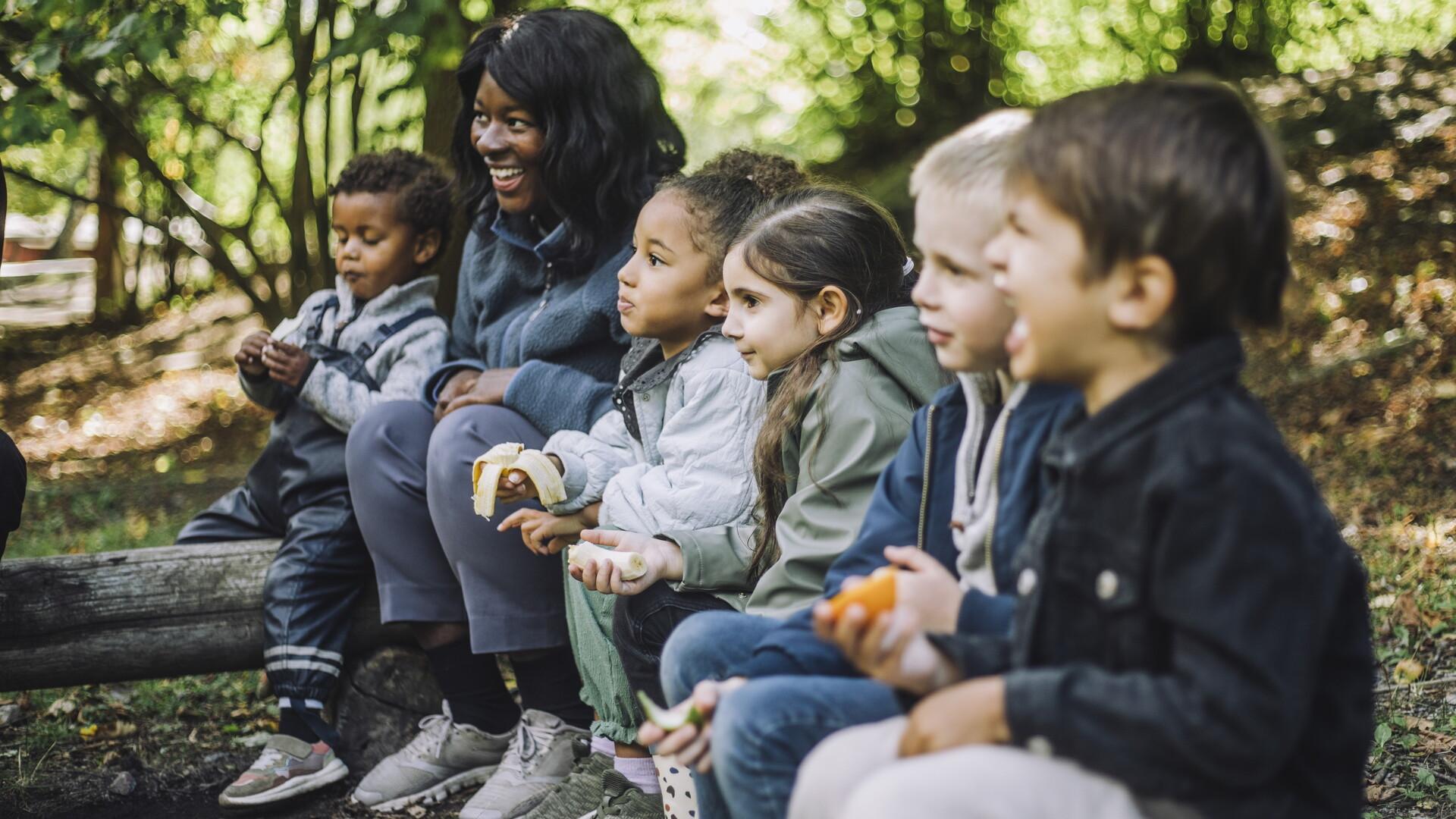 En barnskötare sitter i skogen med en grupp barn.