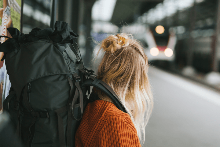 Ung kvinna med en stor ryggsäck spanar läng en tågperrong.