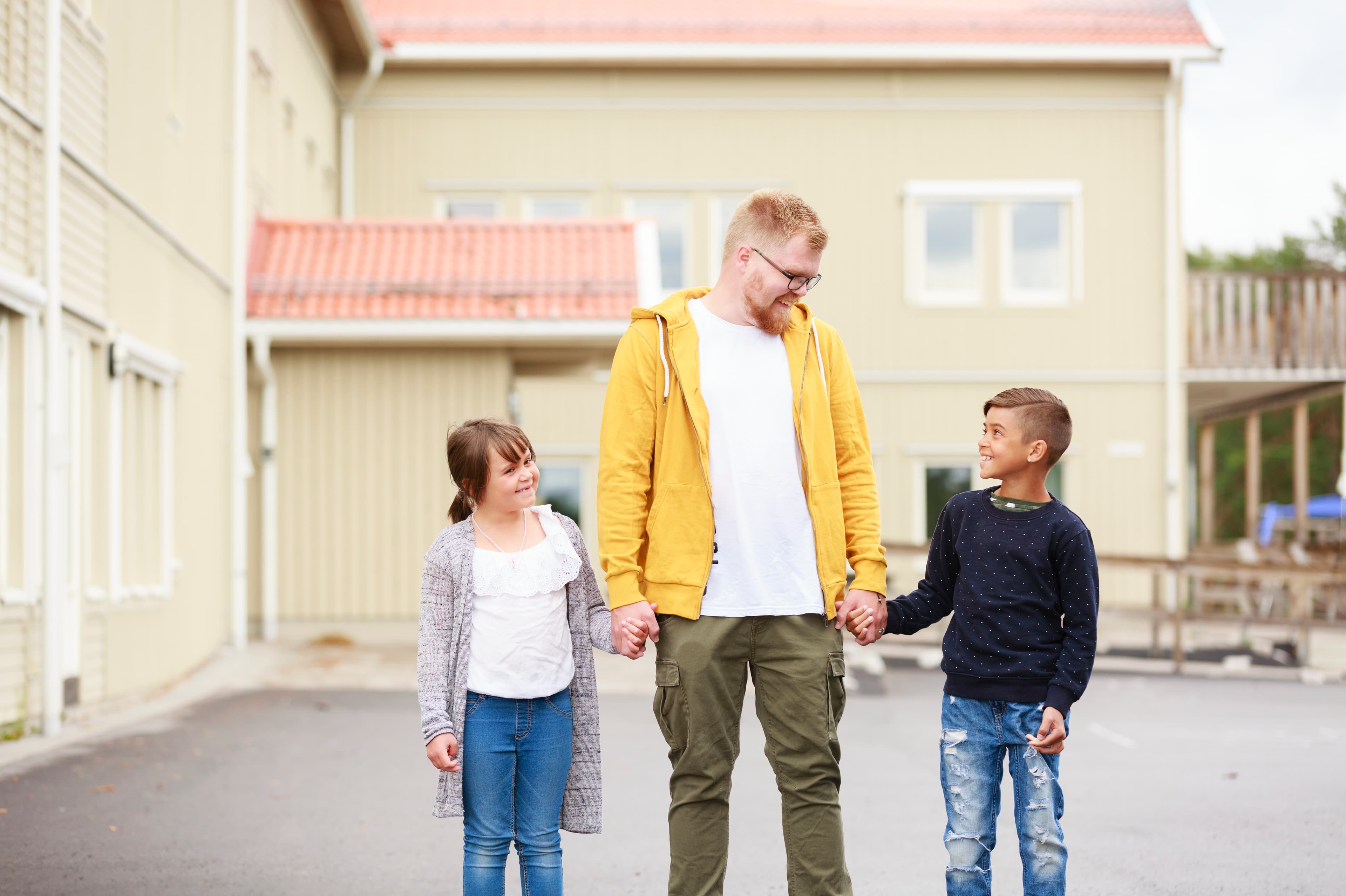 Man står på en skolgård och håller två barn i varsin hand