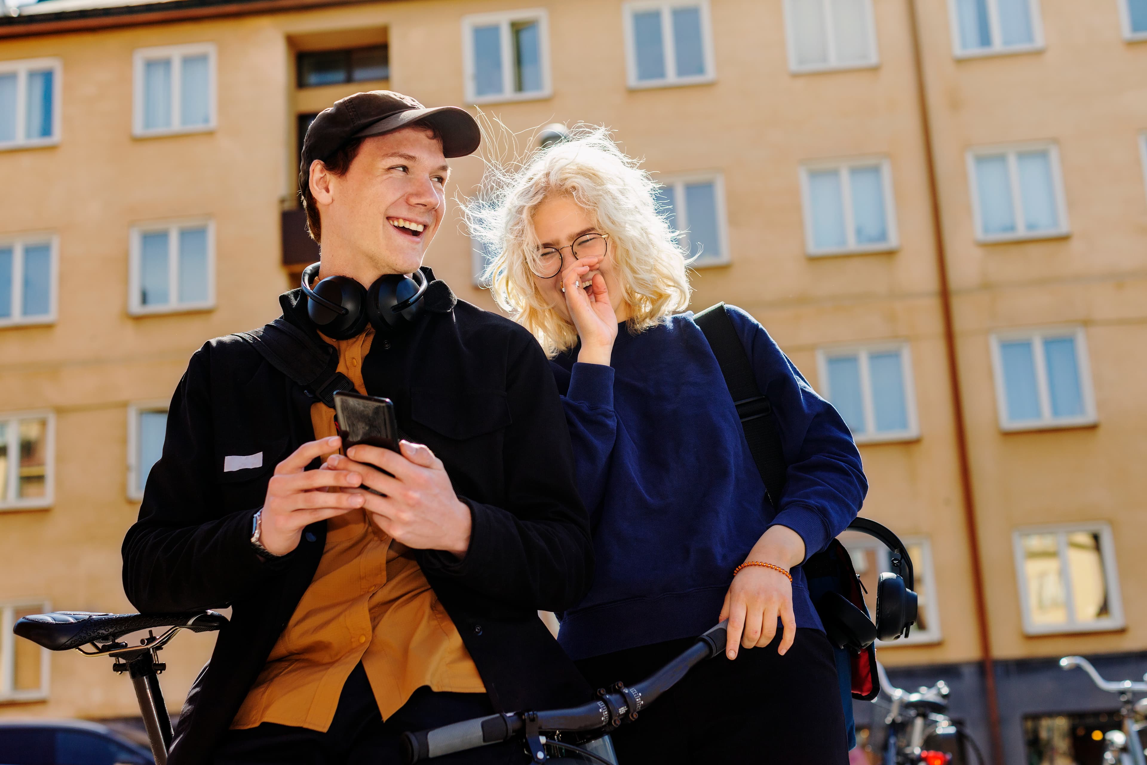En ung man och kvinna står vid sina cyklar, kollar i en telefon och skrattar.