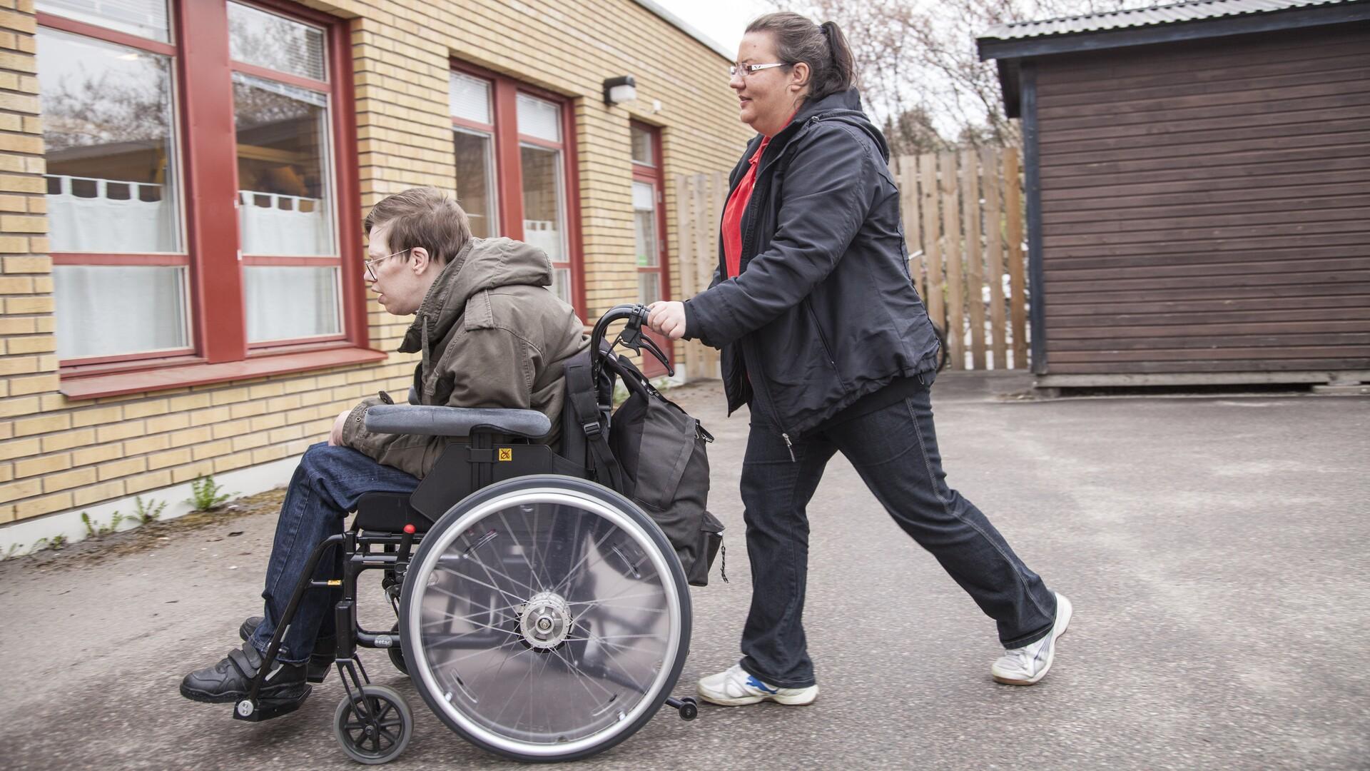Kvinna skjutsar man i rullstol utan för byggnad.