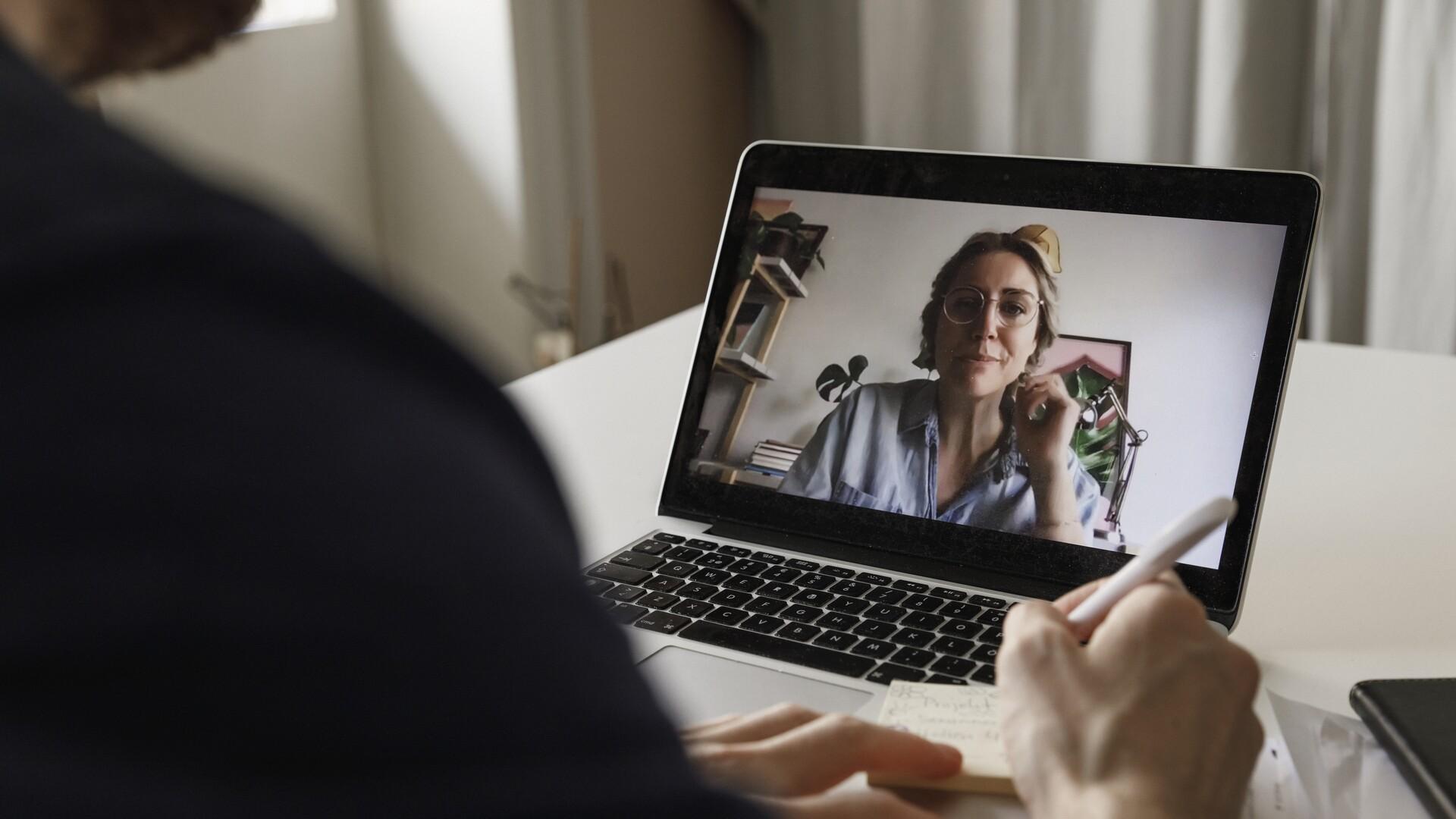 En person sitter i ett möte på datorn med en kvinna på skärmen.
