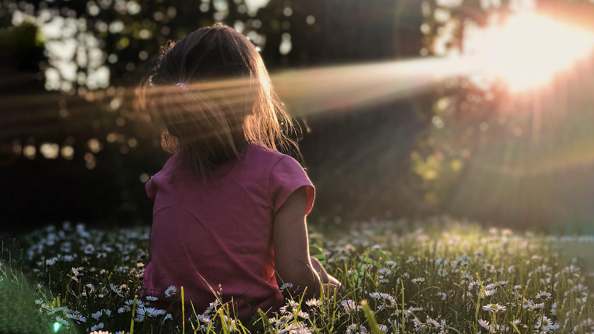 Ett barn sitter på en gräsmatta med ansiktet vänt mot solen.