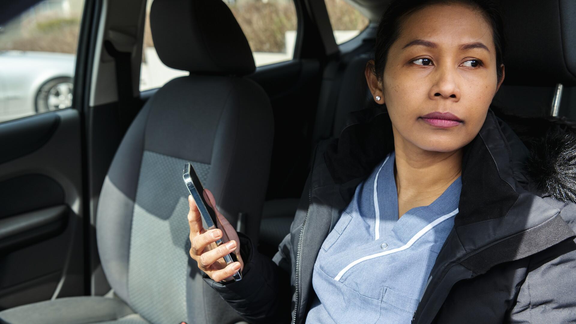 Kvinna med mobiltelefon i handen i en bil.