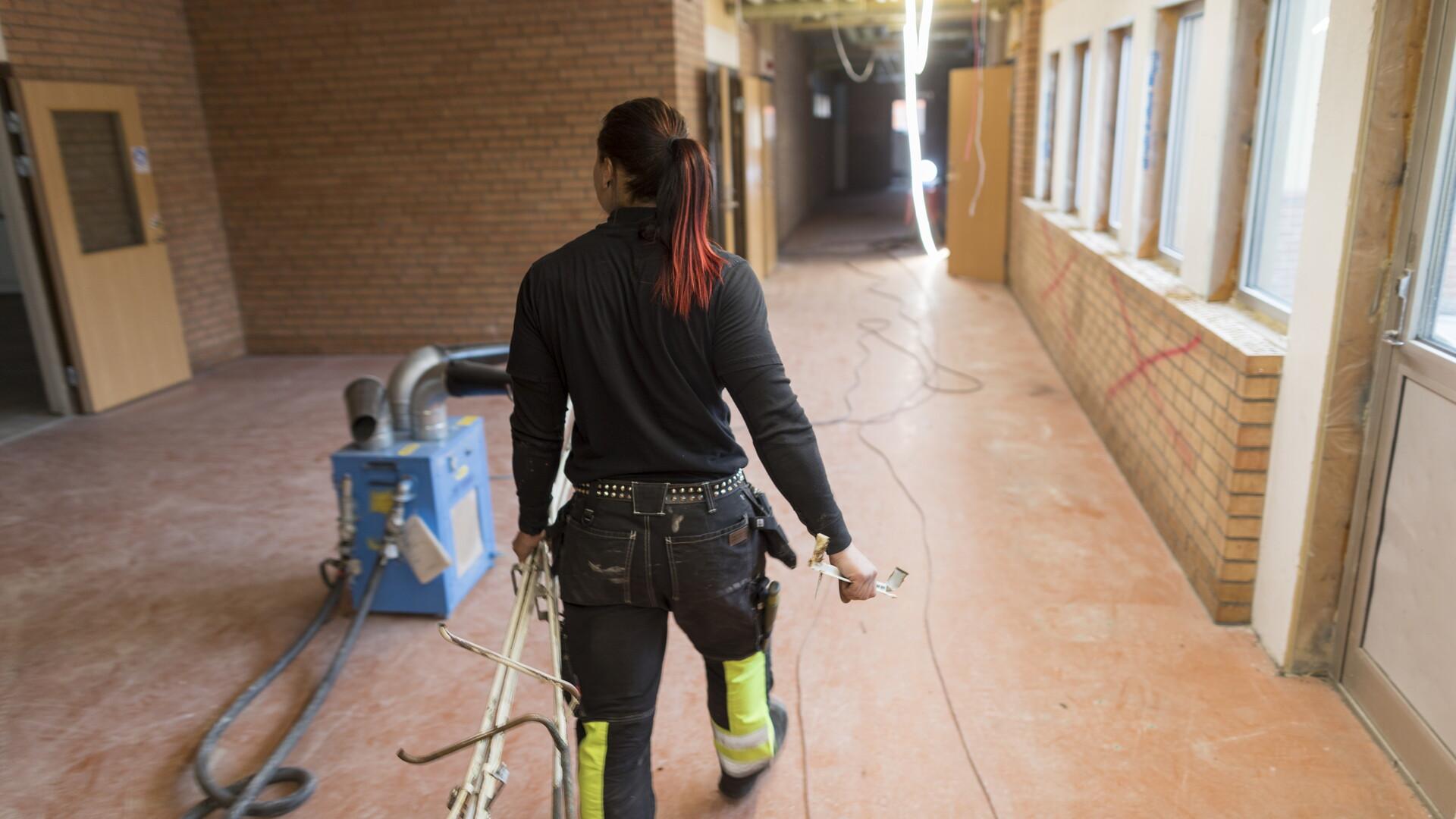 Bild på kvinna i arbetskläder i en korridor med en maskin på golvet.