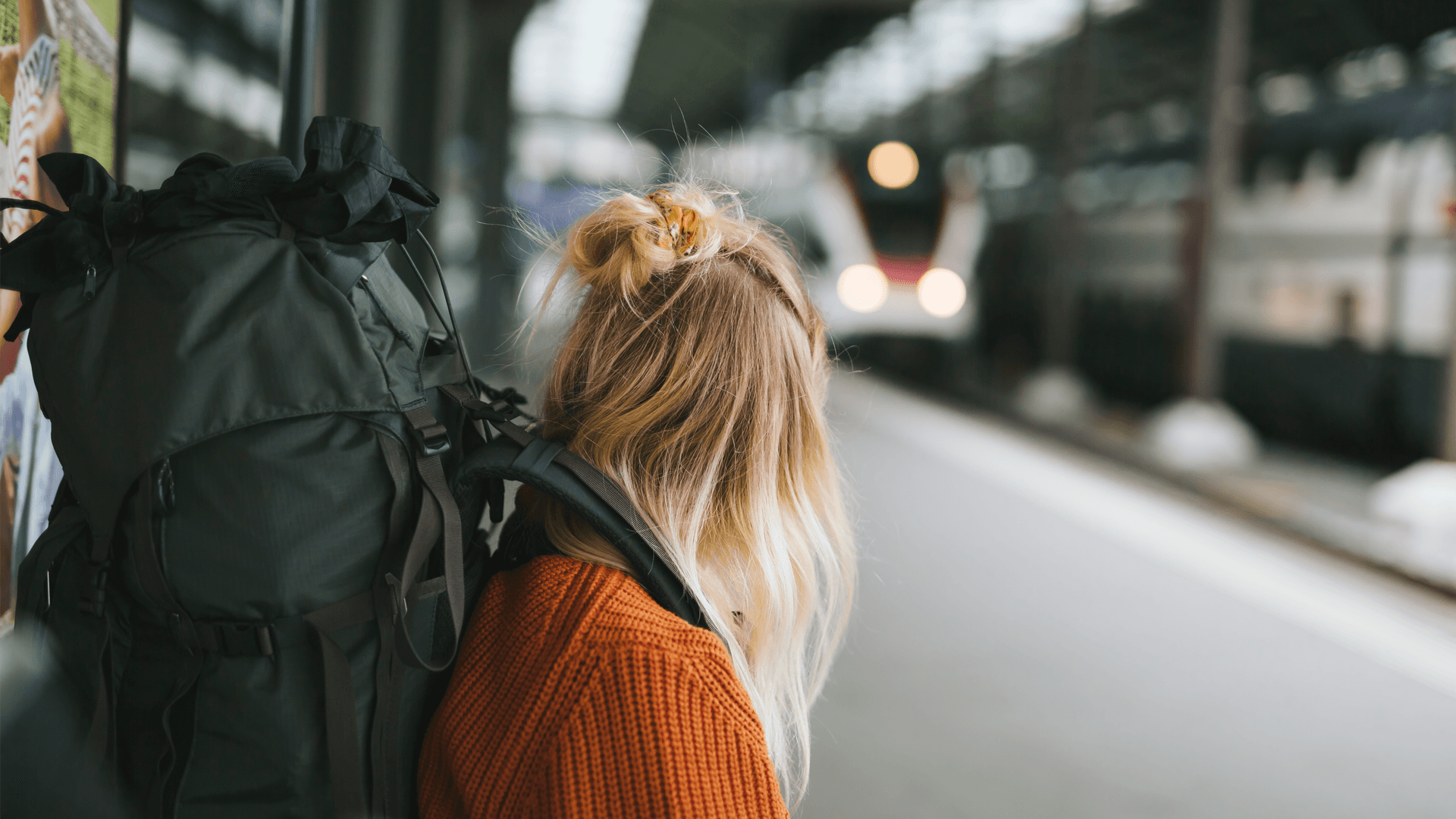 Ung kvinna med stor ryggsäck står på en perrong och väntar på tåget.