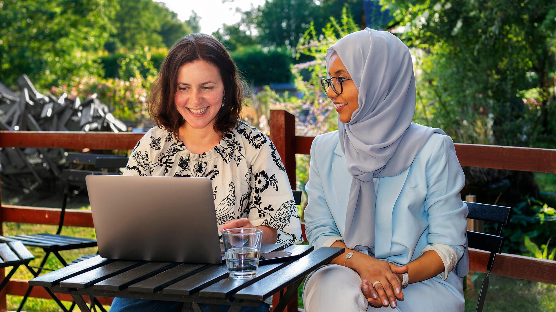 Två kvinnor som pratar med varann utomhus med en laptop.