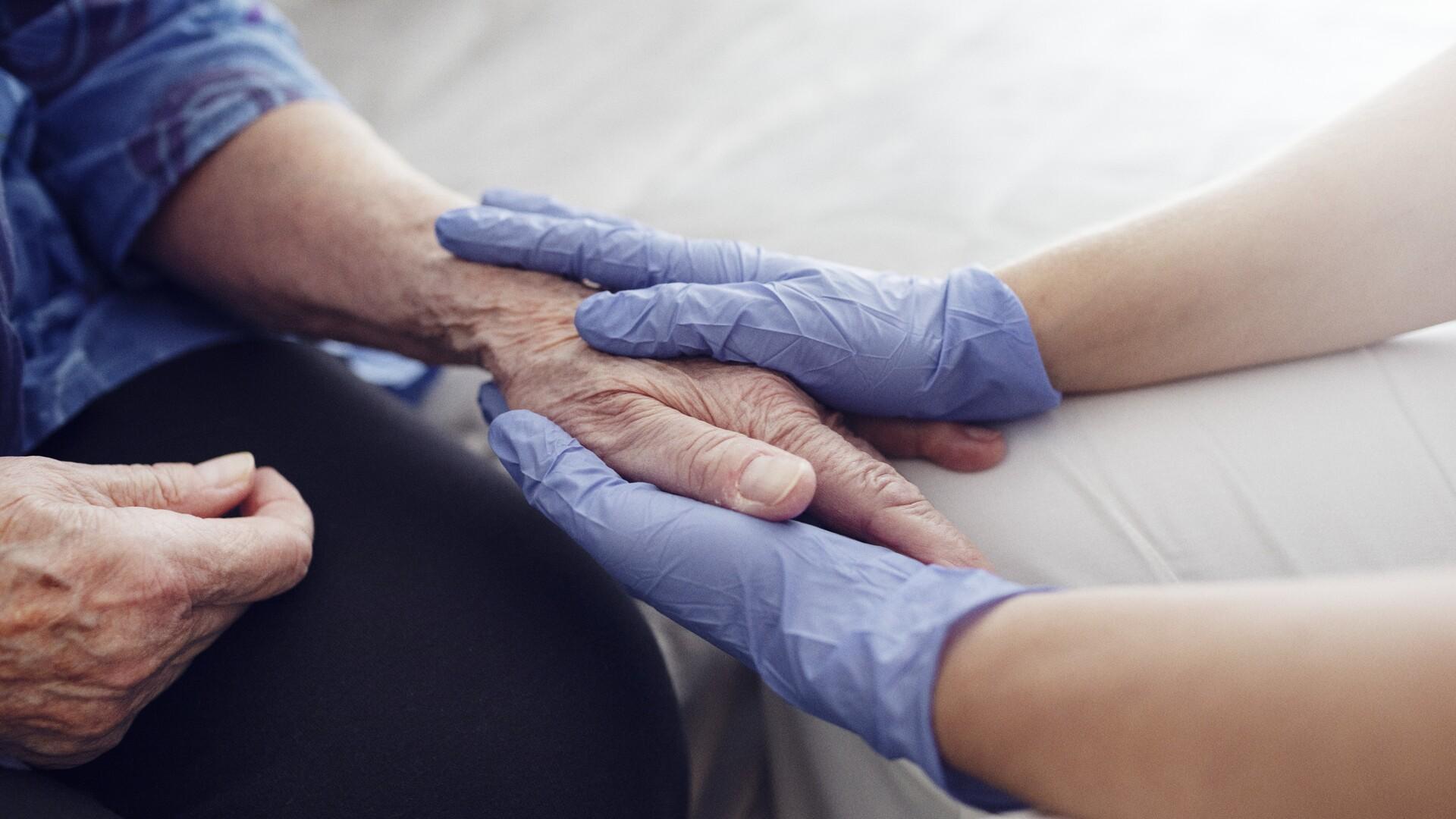 Omvårdare håller en äldre människas hand mellan sina båda händer
