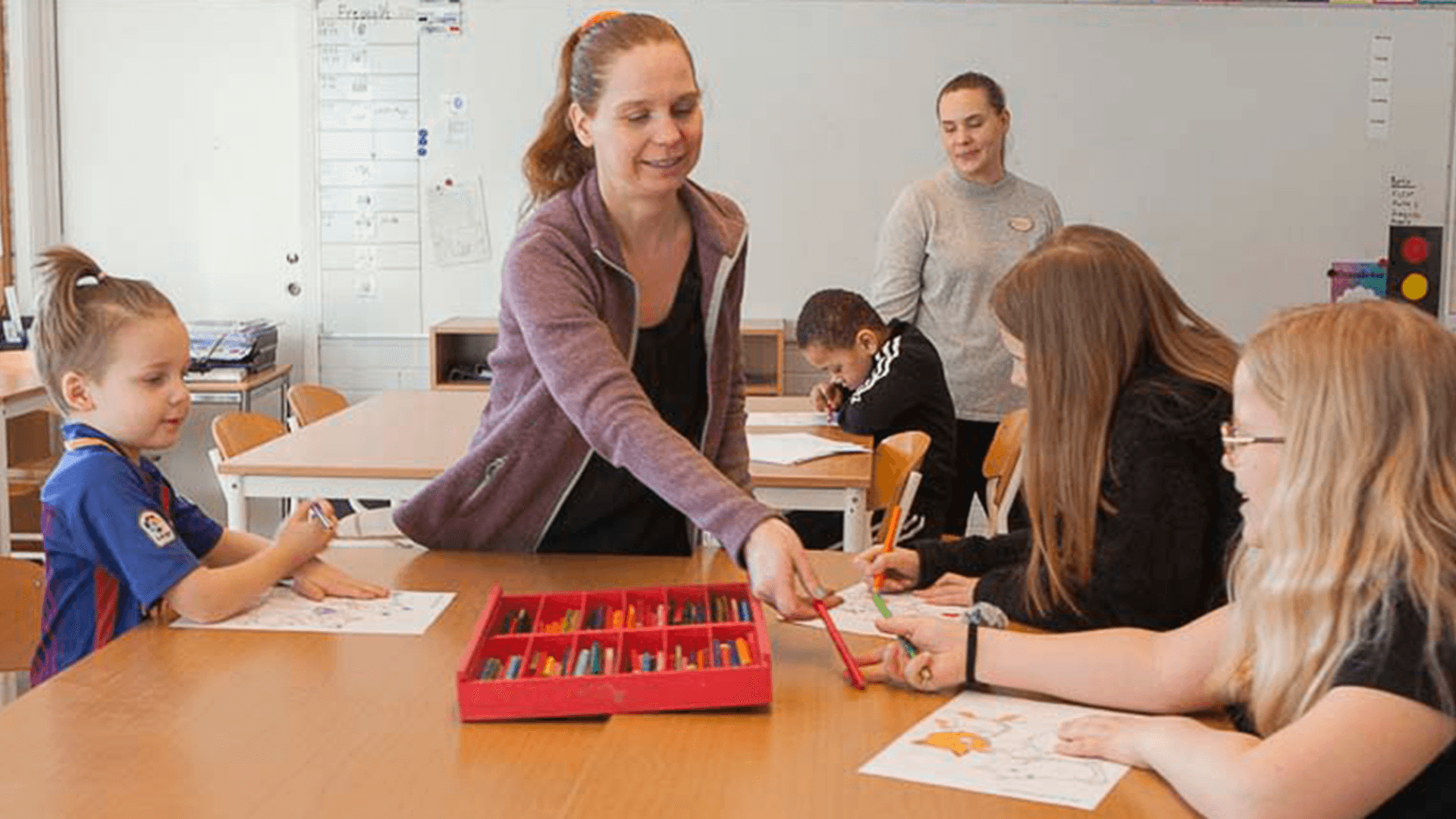 Två kvinnor i ett klassrum hjälper barn. 