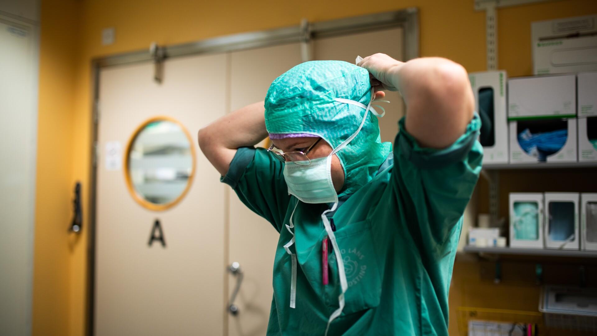 Bild på undersköterska som trär på munskydd utanför operationssal.
