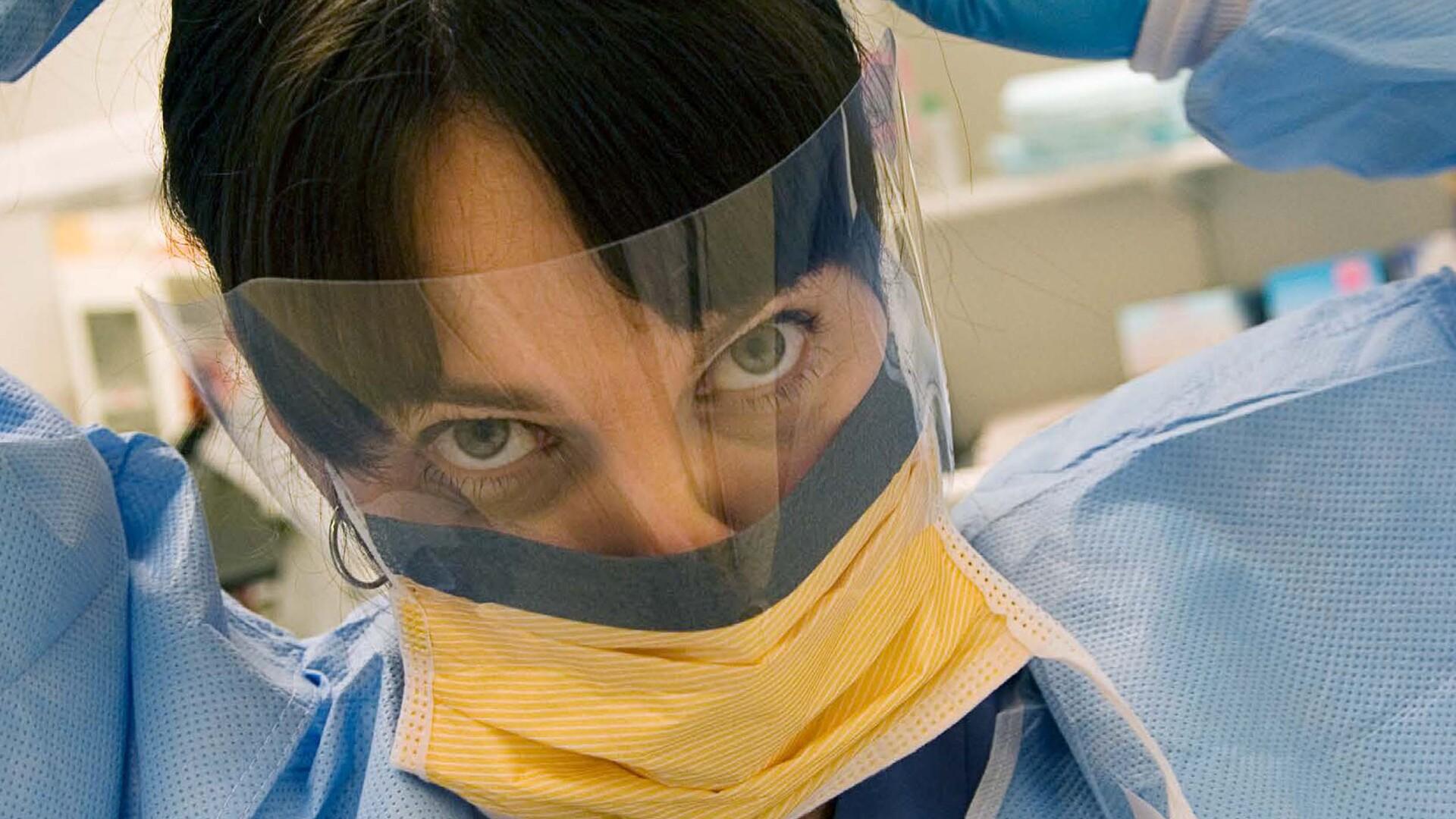 Bild på kvinna med visir och munskydd. 