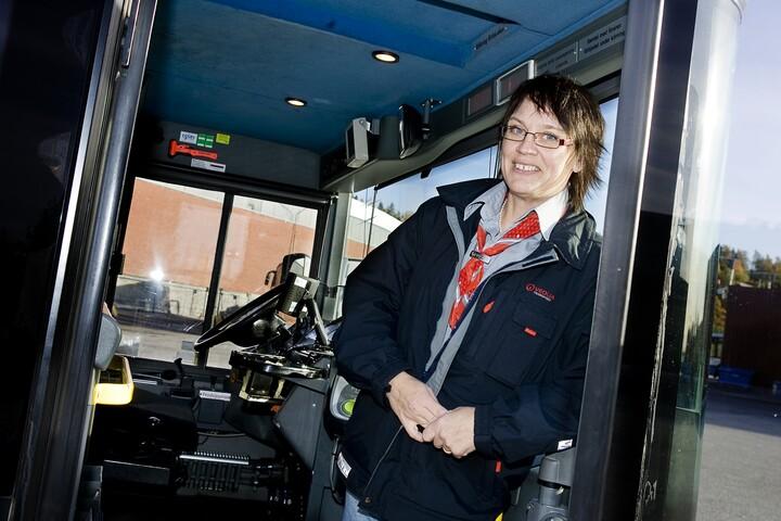 Kvinna står vid förarsätet i en buss. 