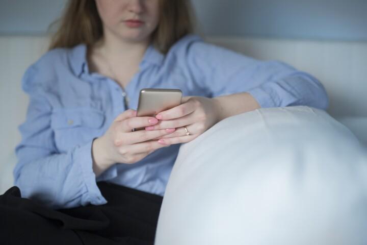 Kvinna sitter i soffan och tittar i mobiltelefon.
