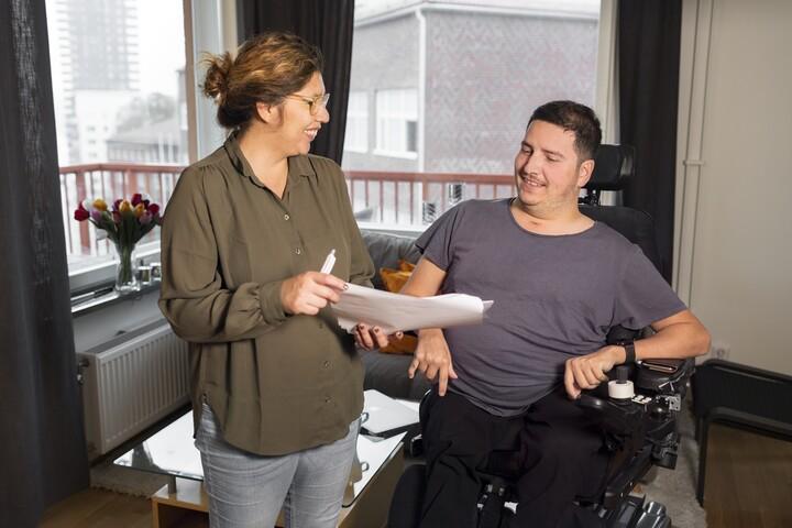 Bild på kvinna som står bredvid man i rullstol. 