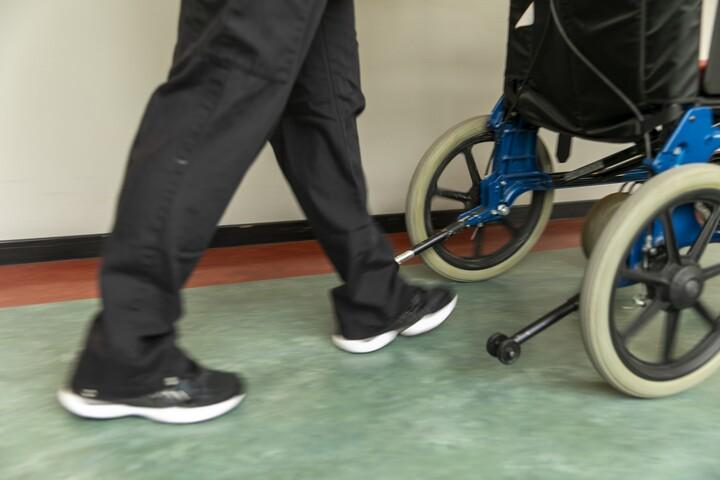 Närbild på skor på person framför rullstol.