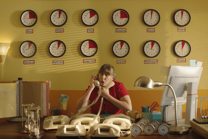 Kvinna under vägg med klockor håller i flera telefonlurar samtidigt.