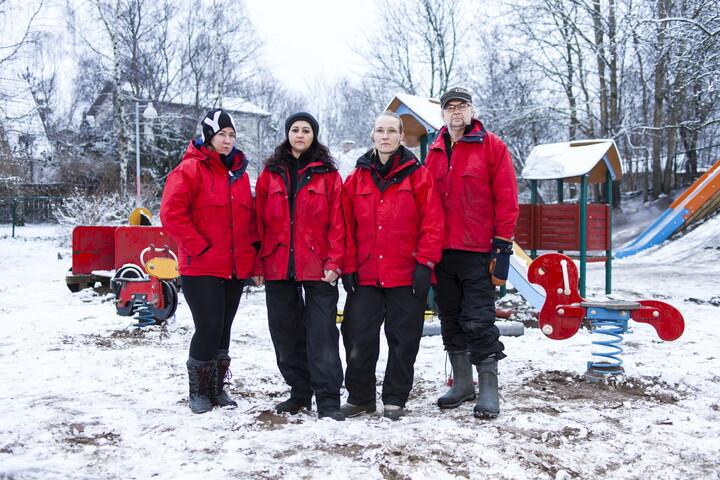 Fyra barnskötare i röda jackor står i en snöig lekpark.