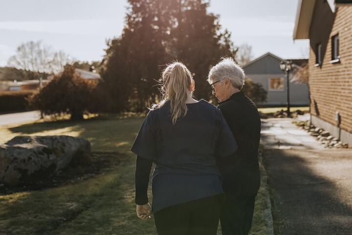 Bild på kvinna som går bredvid äldre kvinna utomhus.