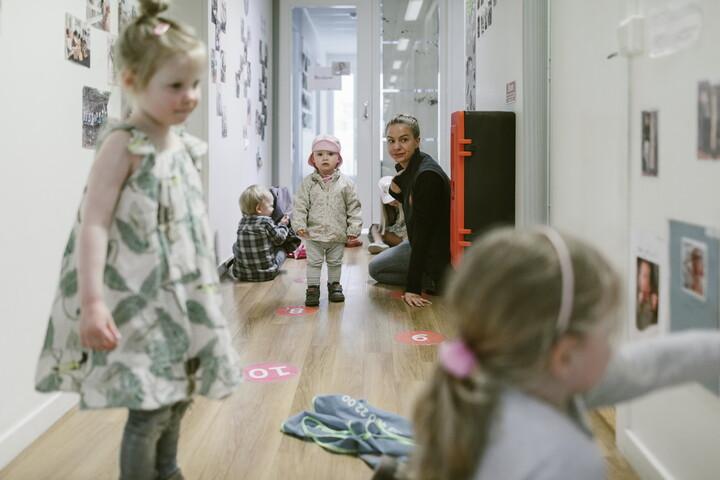 Bild på fyra små barn i korridor och en vuxen som sitter i bakgrunden.