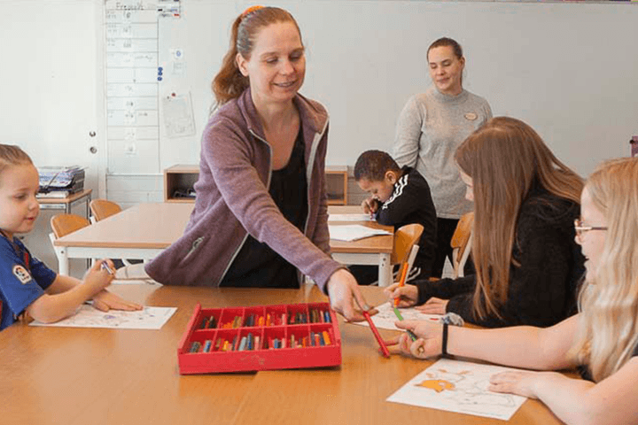 Två kvinnor i ett klassrum hjälper barn. 