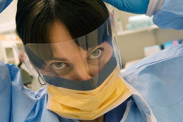 Bild på kvinna med visir och munskydd. 